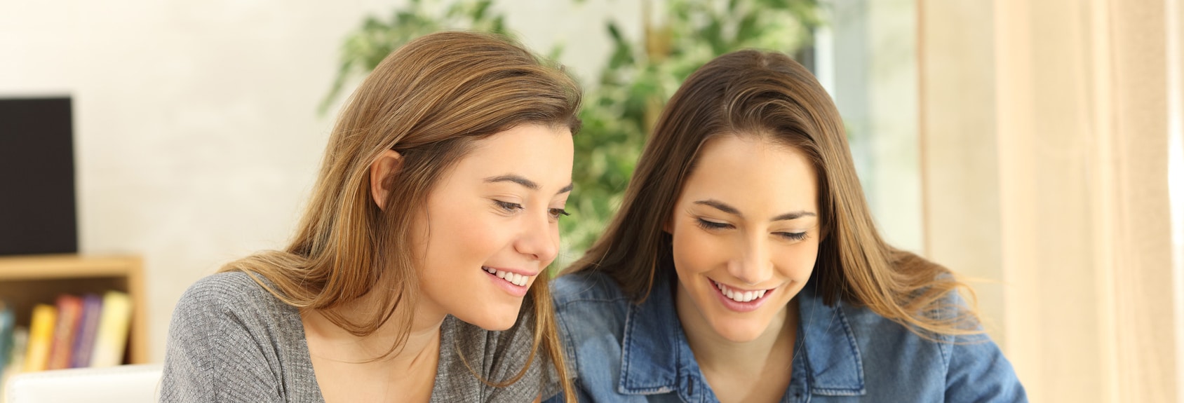 Two students doing homework together and helping each other sitting in a table at home with a homey background